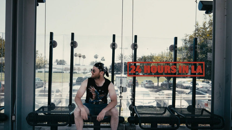 「24 HOURS IN LA」の文字が入った、駅のベンチに座るサングラス姿の男性
