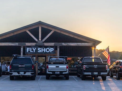 夕暮れの空の下、「FLY SHOP」の看板を掲げたThe Fly Boxの店舗と前に並ぶピックアップトラック